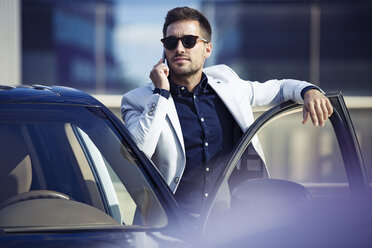 Young businessman standing at his car, talking on the phone - JSRF00074