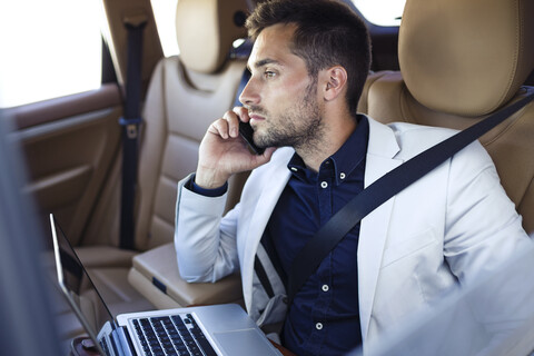 Junger Geschäftsmann arbeitet auf dem Rücksitz eines Autos, lizenzfreies Stockfoto