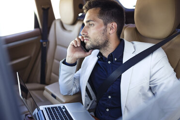 Young businessman working from the backseat of a car - JSRF00088