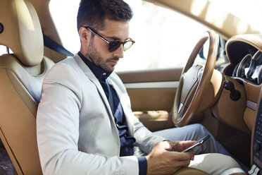 Young businessman sitting in car, using smartphone - JSRF00090