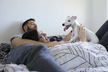 Couple lying on bed cuddling dog - ZEDF01779