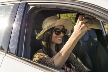 Smiling young woman sitting in a car taking selfie with cell phone - FBAF00191