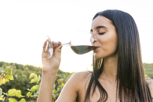 Italien, Toskana, Siena, junge Frau trinkt Rotwein in einem Weinberg bei Sonnenuntergang - FBAF00209