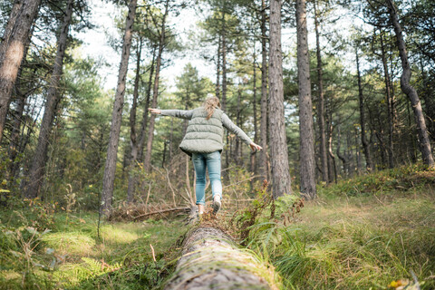 Kleines Mädchen balanciert auf einem Baumstamm im Wald, lizenzfreies Stockfoto