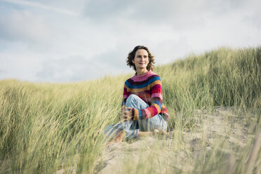 Mature woman relaxing on the beach, sitting in the dunes - MOEF01572