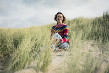 Mature woman relaxing on the beach, sitting in the dunes - MOEF01573