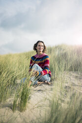 Mature woman relaxing on the beach, sitting in the dunes - MOEF01574