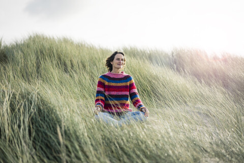 Ältere Frau entspannt sich am Strand, sitzt in den Dünen, lizenzfreies Stockfoto