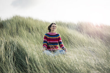 Mature woman relaxing on the beach, sitting in the dunes - MOEF01575