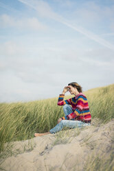 Mature woman relaxing on the beach, sitting in the dunes - MOEF01578