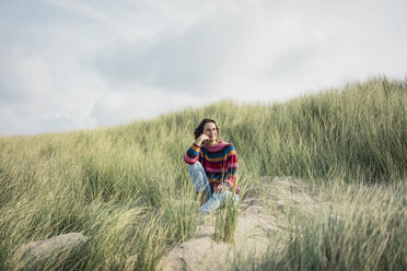 Mature woman relaxing on the beach, sitting in the dunes - MOEF01579