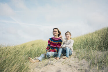 Mutter und Tochter sitzen auf einer Stranddüne, das Mädchen zeigt in die Ferne und lächelt - MOEF01580
