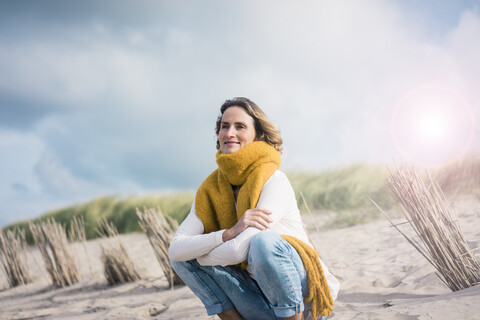 Ältere Frau hockt in den Dünen und genießt den Wind, lizenzfreies Stockfoto