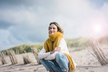 Mature woman crouching in the dunes, enjoying the wind - MOEF01590