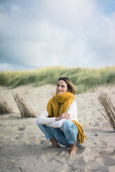 Mature woman crouching in the dunes, enjoying the wind - MOEF01591