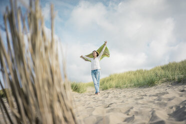 Mature woman holding flapping scarf in the wind, relxiang in the dunes - MOEF01598