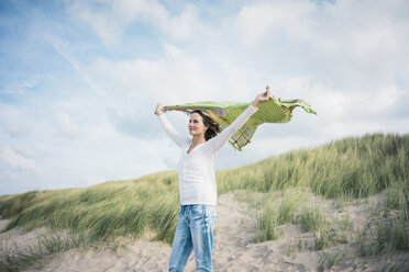 Mature woman holding flapping scarf in the wind, relxiang in the dunes - MOEF01600