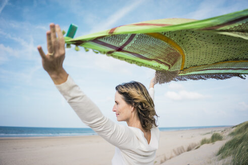 Mature woman holding flapping scarf in the wind, relxiang in the dunes - MOEF01601