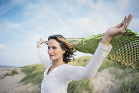 Mature woman holding flapping scarf in the wind, relxiang in the dunes stock photo