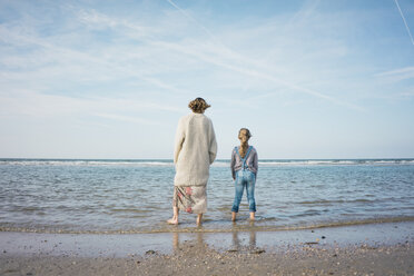 Mother and daughter standing on the beach, looking at the sea, rear view - MOEF01607