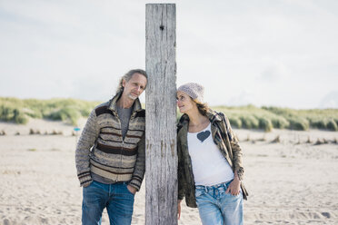 Mature couple on the beach, leaning on wood pole - MOEF01609