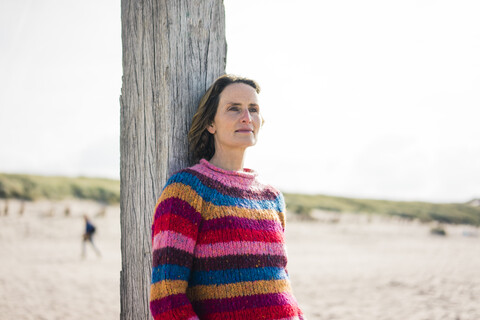 Reife Frau entspannt sich am Strand und stützt sich auf eine Stange, lizenzfreies Stockfoto