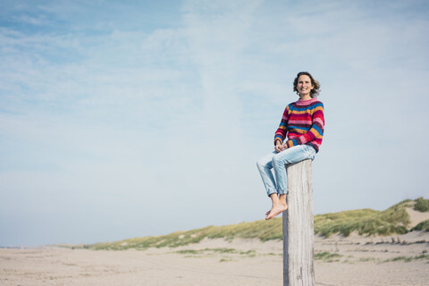 Ältere Frau sitzt auf einem Holzpfahl am Strand, lizenzfreies Stockfoto