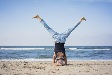 Mature woman doing a headstand on the beach - MOEF01631