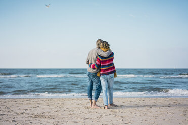 ein hübsches Paar, das am Strand steht, die Arme um sich legt und auf das Meer schaut - MOEF01633