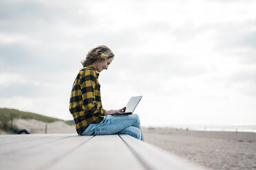 Ältere Frau sitzt auf der Promenade am Strand und benutzt einen Laptop - MOEF01637