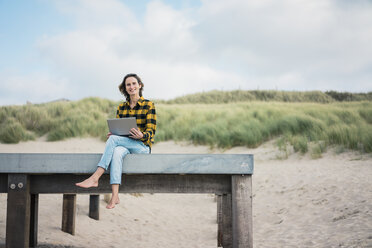 Mature woman sitting on boardwalk at the beach, using laptop - MOEF01639