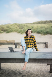 Ältere Frau sitzt auf der Promenade am Strand und benutzt einen Laptop - MOEF01640