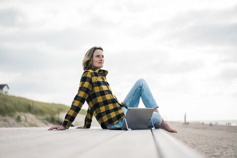 Mature woman sitting on boardwalk at the beach, using laptop stock photo