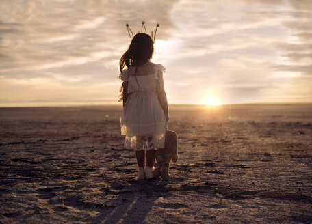 Rückansicht eines Mädchens mit Stofftier auf einem Feld vor einem bewölkten Himmel bei Sonnenuntergang - CAVF56017