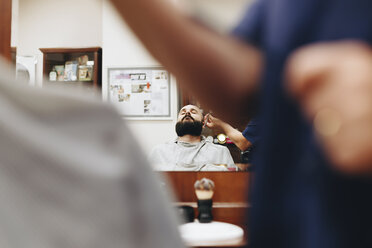 Mittelteil eines Friseurs, der einem Mann den Bart schneidet und sich im Spiegel eines Salons spiegelt - CAVF56023