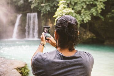 Rückansicht eines Mannes, der mit seinem Smartphone einen Wasserfall fotografiert - CAVF56055