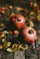 Hohe Winkelansicht von Granatäpfeln mit Beeren und Blättern auf Holztisch - CAVF56068