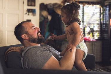 Seitenansicht des Vaters, der mit seiner Tochter spielt, während er zu Hause auf dem Sofa sitzt - CAVF56091