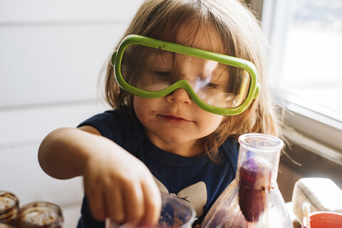 Nahaufnahme eines Mädchens, das eine Schutzbrille trägt, während es zu Hause Essen in der Hand hält, lizenzfreies Stockfoto