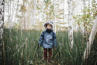 Portrait of boy wearing hooded jacket while standing amidst forest - CAVF56133