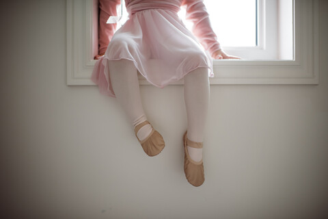 Tiefschnitt eines Mädchens im Ballettkostüm, das zu Hause auf der Fensterbank sitzt, lizenzfreies Stockfoto