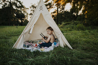 Boy playing with toy airplane in tent on grassy field at park - CAVF56150