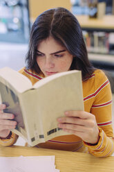 Frau liest ein Buch, während sie am Tisch in der Bibliothek sitzt - CAVF56177