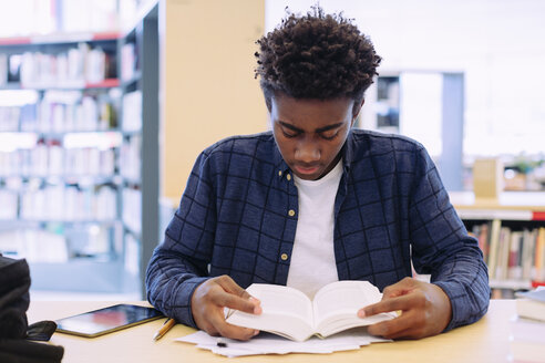 Mann liest ein Buch, während er am Tisch in der Bibliothek sitzt - CAVF56179