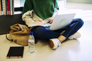 Tiefschnitt einer Frau, die in einer Bibliothek auf dem Boden sitzend einen Laptop benutzt - CAVF56187