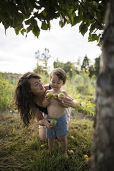 Mutter betrachtet ihren Sohn ohne Hemd, der Früchte im Gemeinschaftsgarten hält - CAVF56260