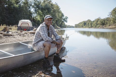Porträt eines lächelnden Mannes, der auf einem Boot am Seeufer sitzt, lizenzfreies Stockfoto