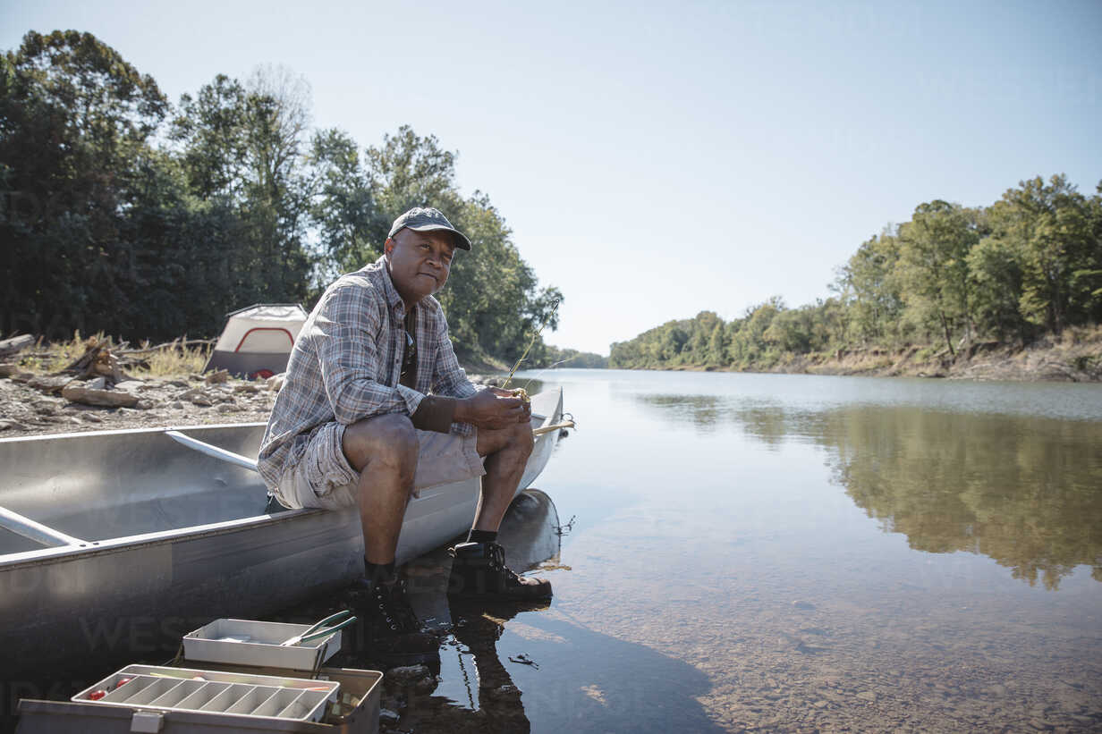 Man holding fishing rod while sitting on boat at lakeshore stock photo