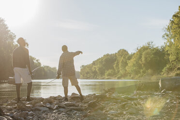Rückansicht von männlichen Freunden mit Angelruten, die am Seeufer stehen, gegen den Himmel an einem sonnigen Tag - CAVF56283