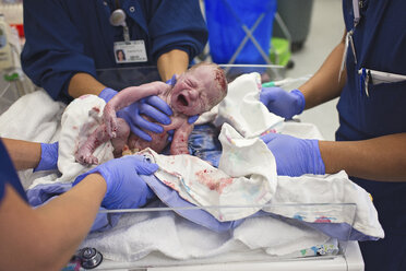 Ärzte in der Mitte, die einen neugeborenen Jungen in einer Krippe im Krankenhaus halten - CAVF56303